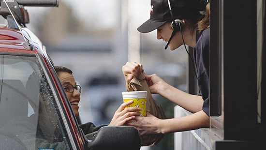 Quick service restaurant drive thru employee handing food and drinks to a customer in their car on a rainy day.