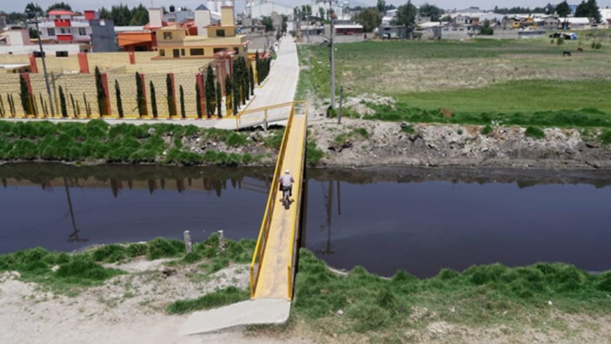 A cyclist rides across a narrow yellow bridge spanning a river