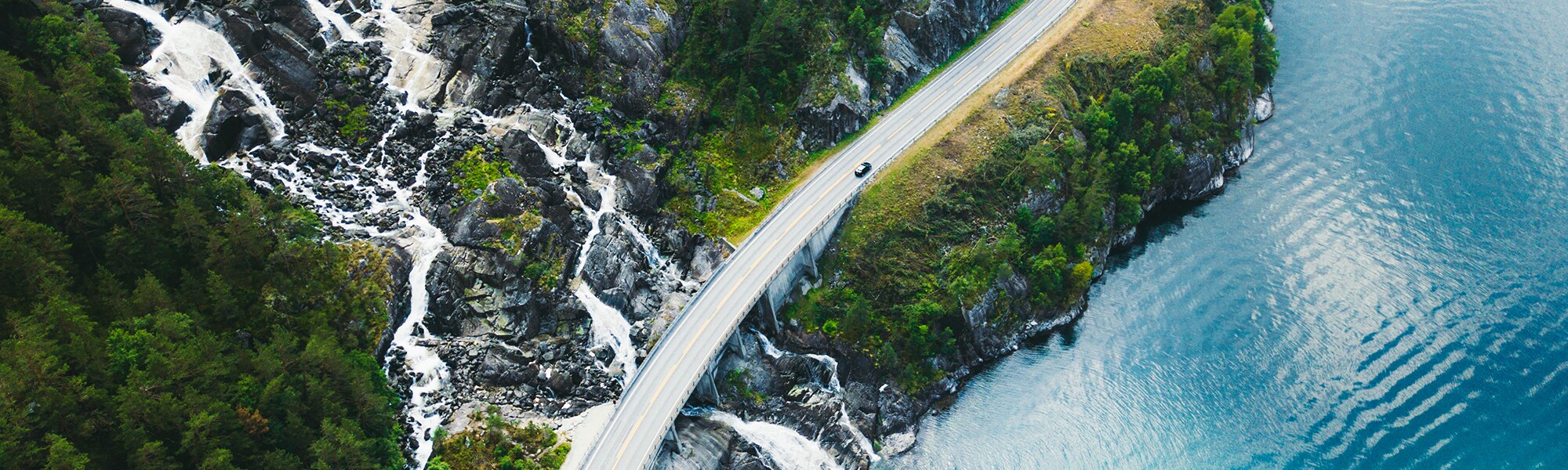 View from above of a road with a car driving along a body of water